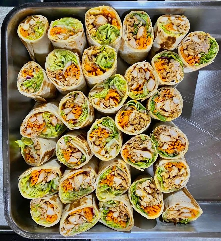A tray of chicken wraps with lettuce and grated carrot, cut in half